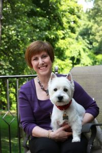 Doctor Debra Horowitz holding her white West Highland Terrier dog with green trees in background