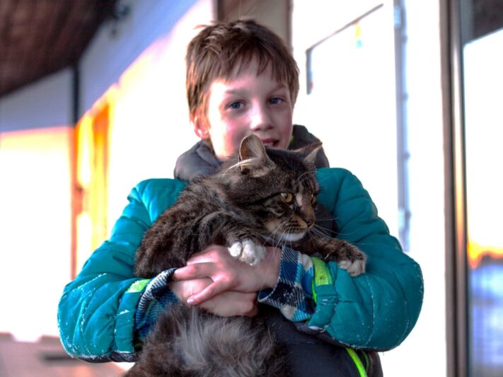 Boy in coat holding a tabby cat.