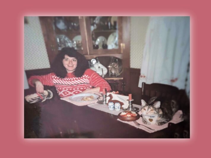 A retro photo of a smiling woman at a dining table with her cat.