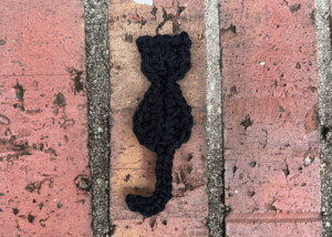 finished Black Cat Crochet Applique against a brick background